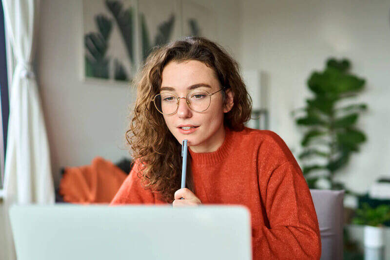 a student holds a pen and looks at her open laptop as she studies for the ACT