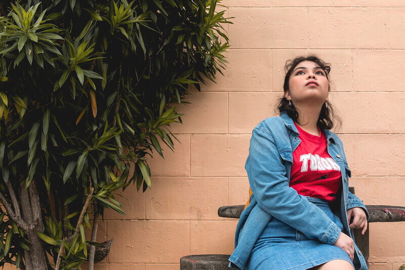 A young woman sitting outside looking up.