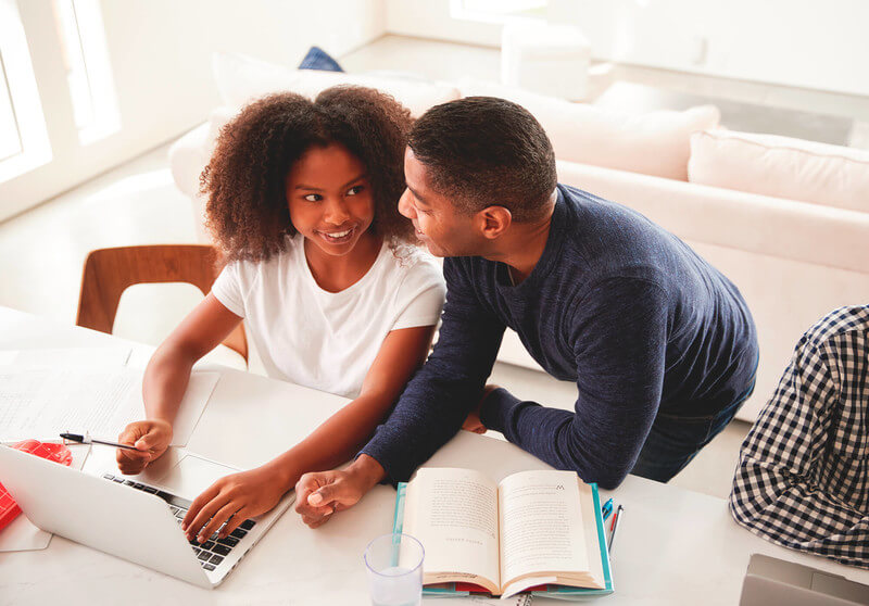 a dad and daughter look at college costs on a laptop computer