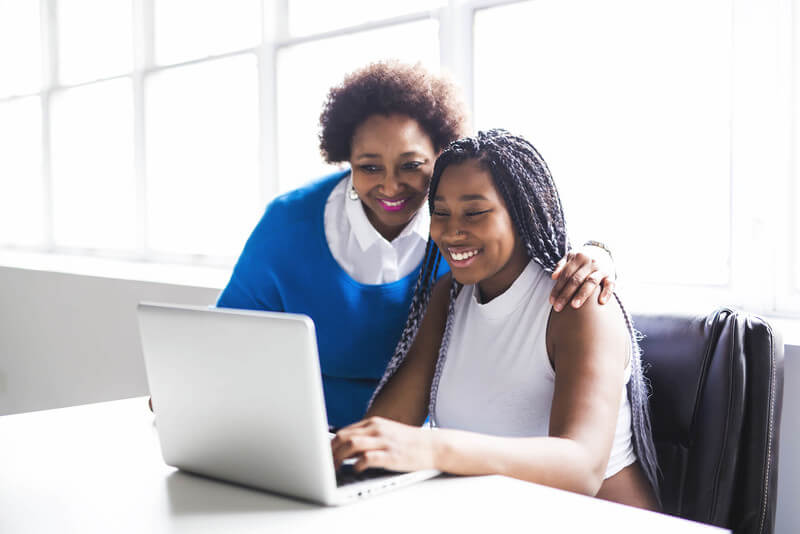 a mother and daughter look at a laptop and financial aid application