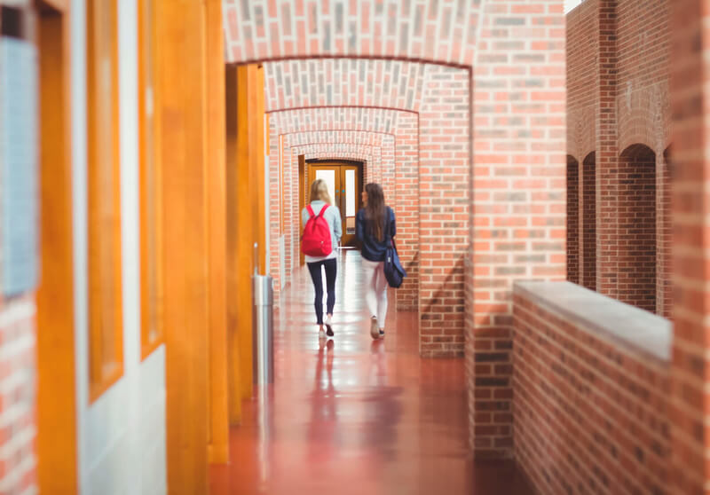 two female students walk down a long hallway ay college