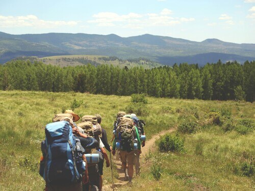 a group hiking through an open pasture with mountains in the background